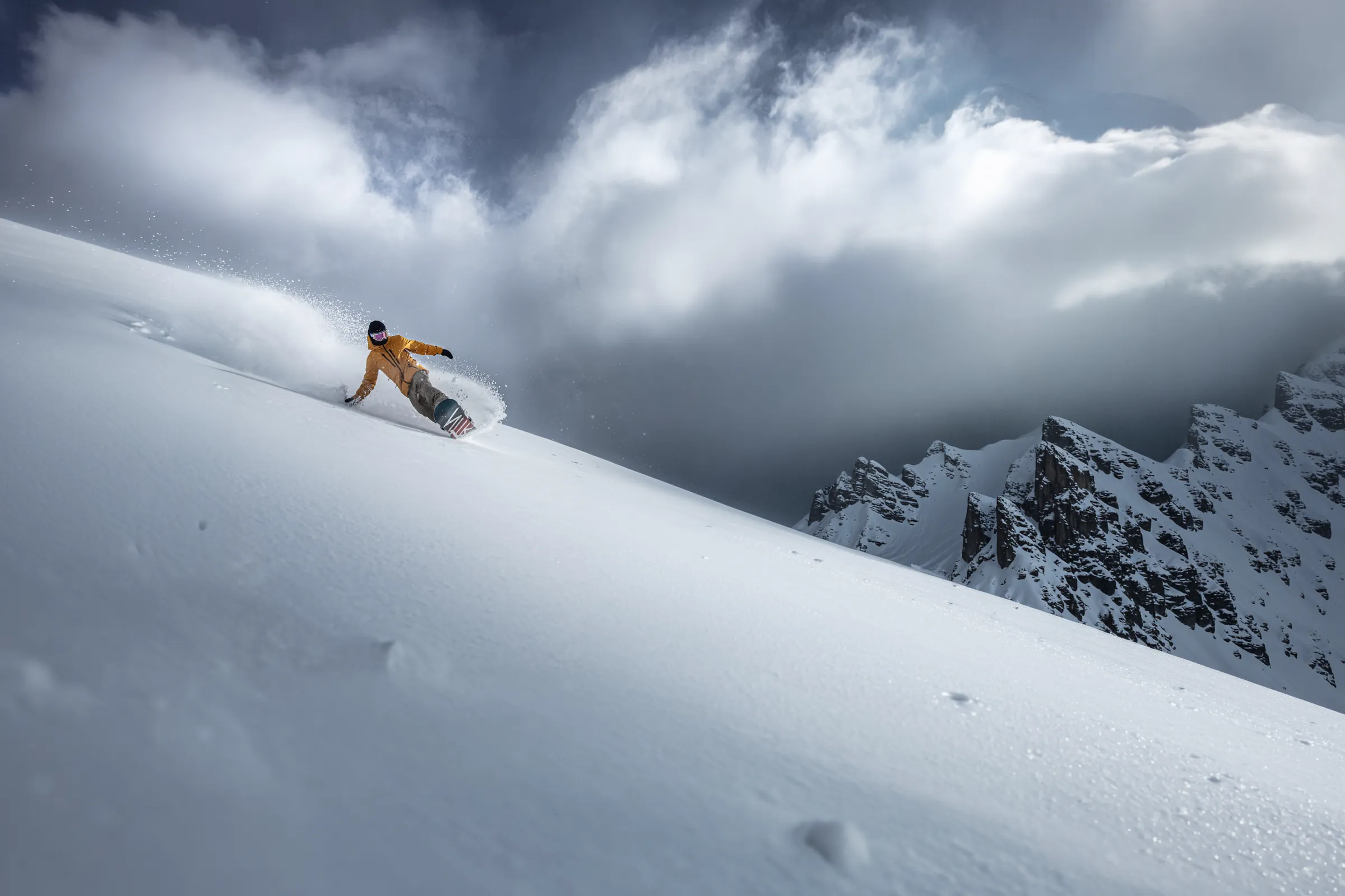 Uno snowboarder che traccia curve nella neve polverosa fresca sotto una cresta rocciosa